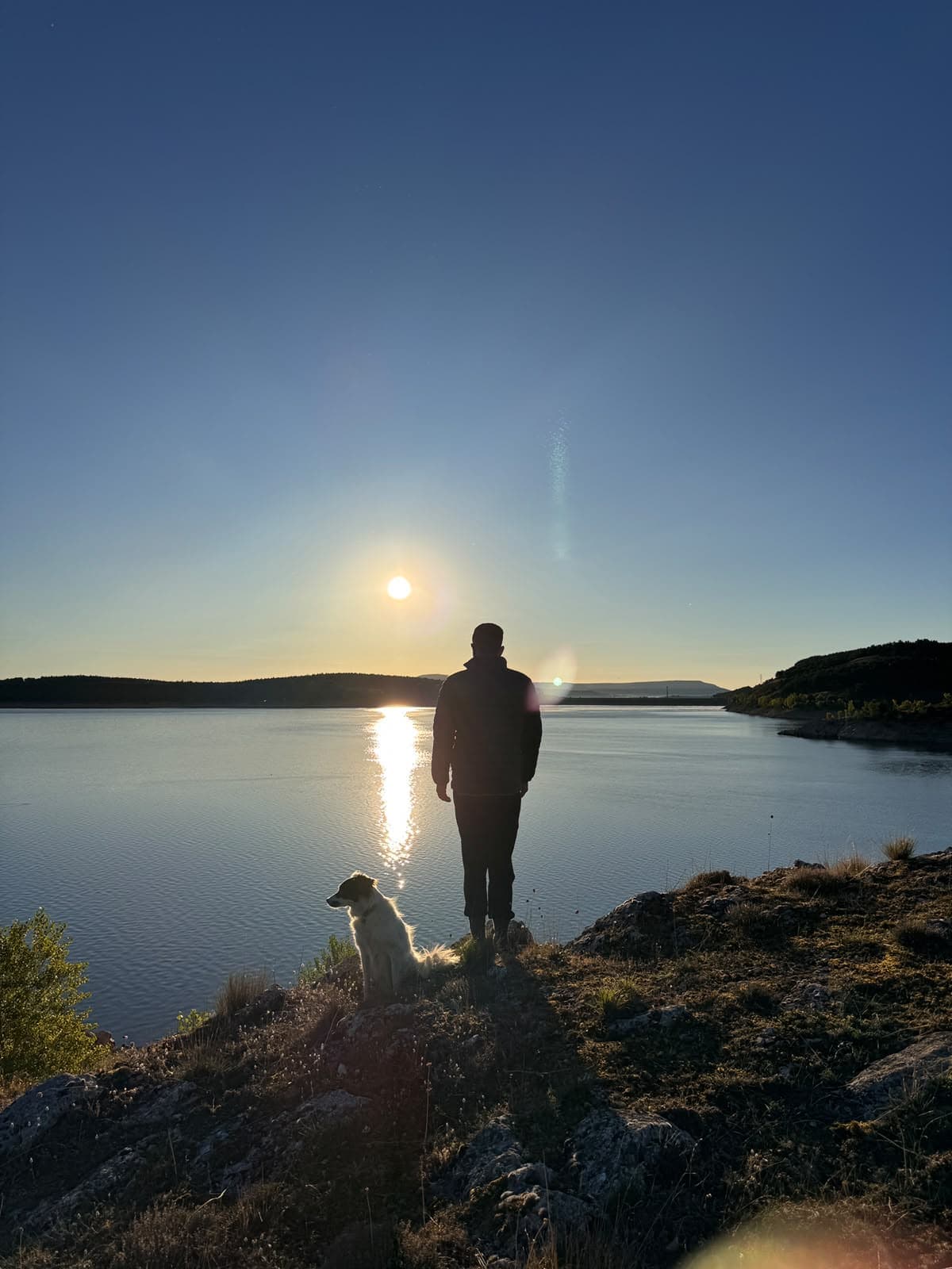 Silhouette of Miguel and a dog on a rock above a lake at sunset